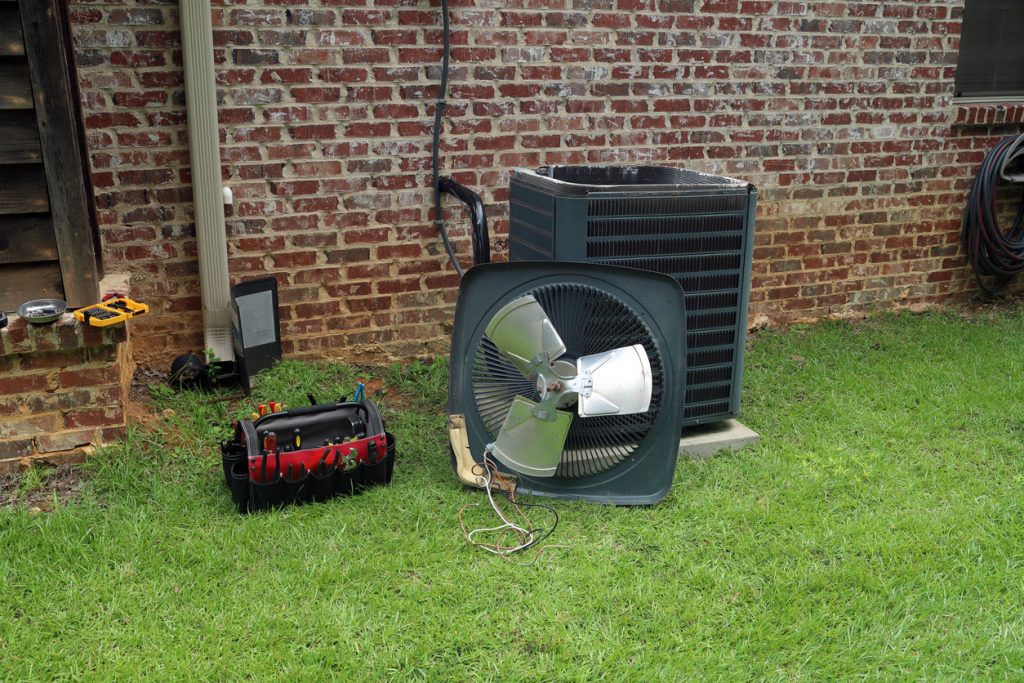 Air Conditioner compressor condenser coil with fan and tools being worked on next to a brick house for repair maintenance